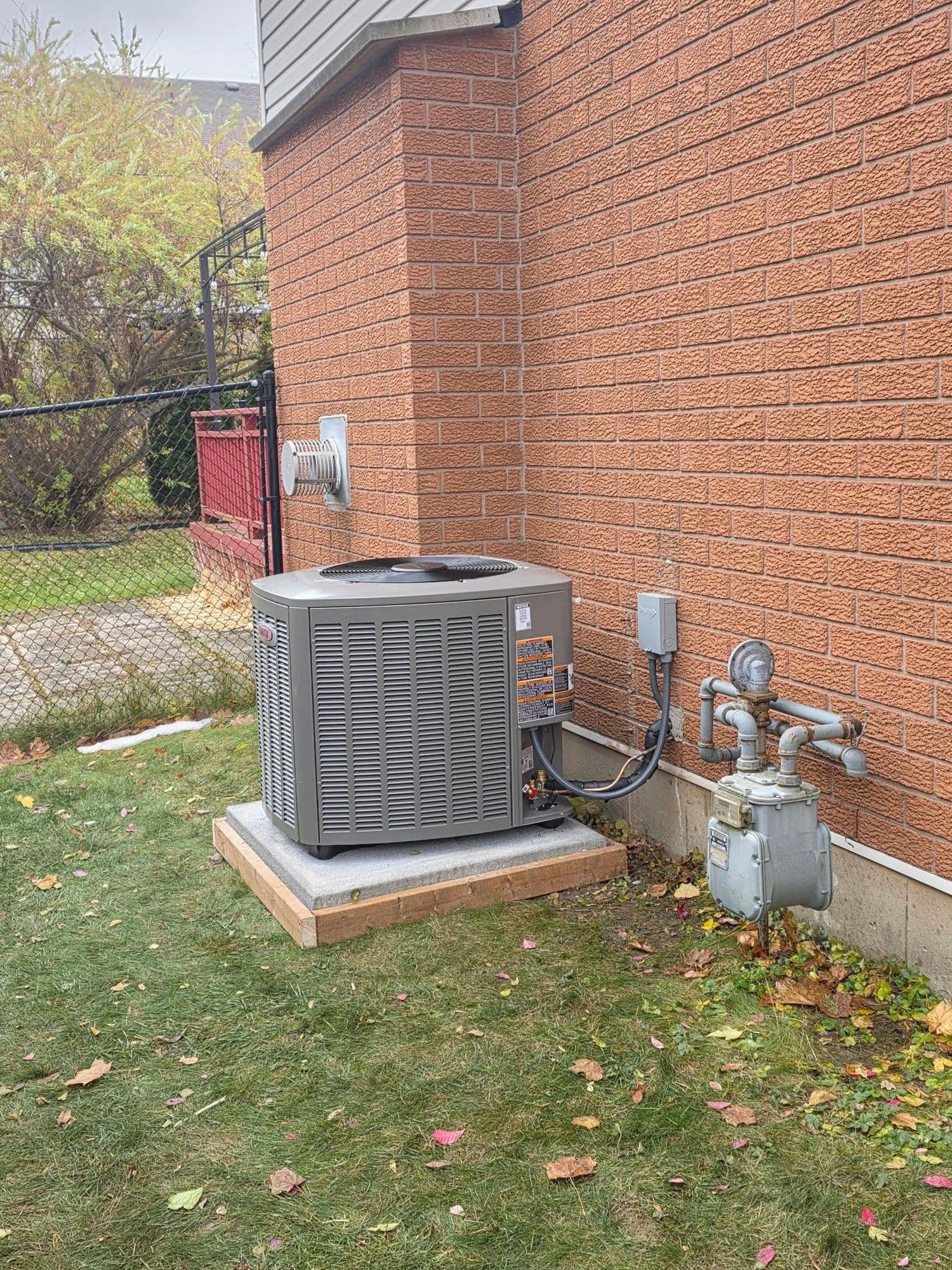 Newly installed outdoor AC condenser on a concrete pad next to a brick home in Niagara