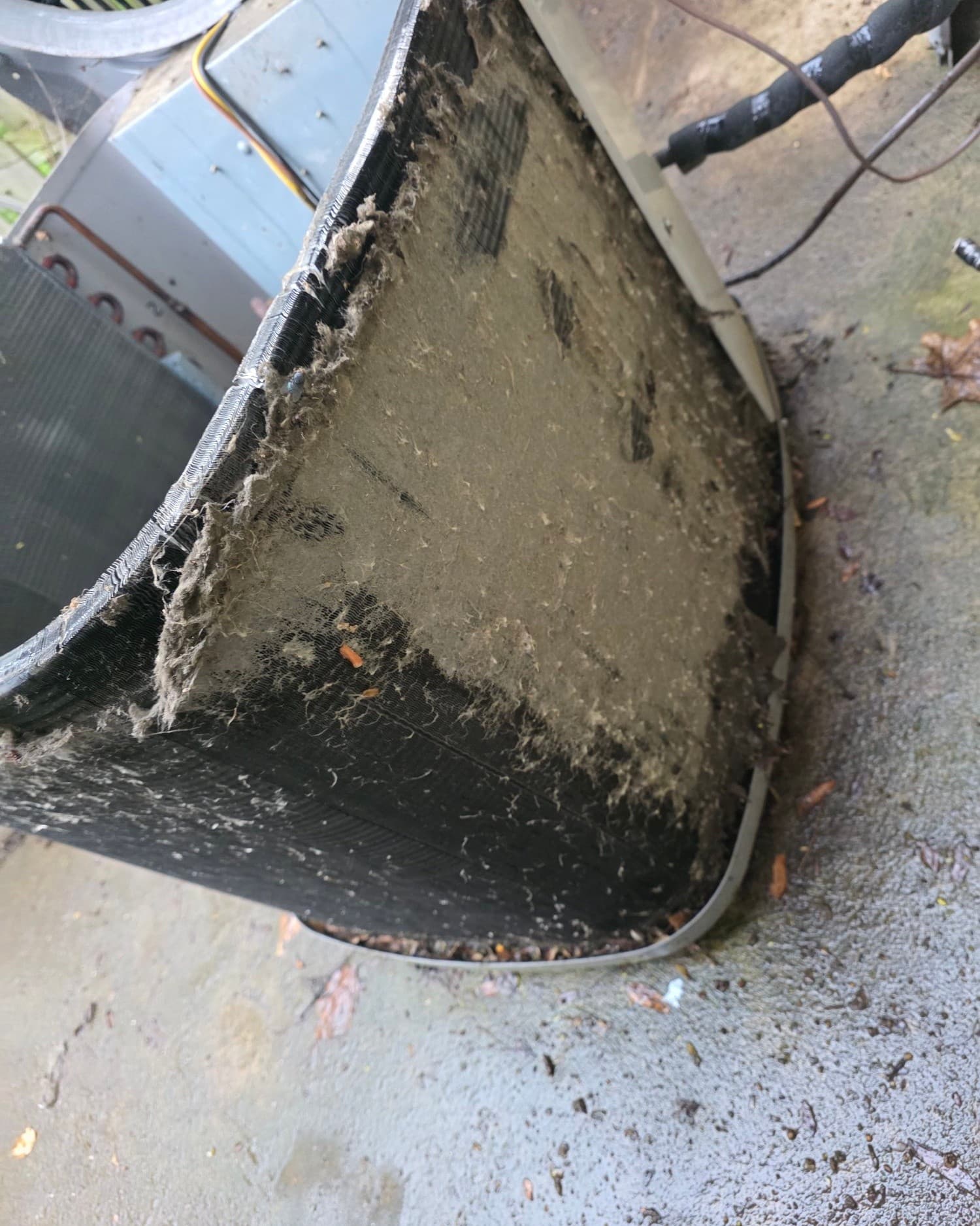Close-up of an outdoor AC condenser coil matted with years of lint and dirt, side panel removed for service